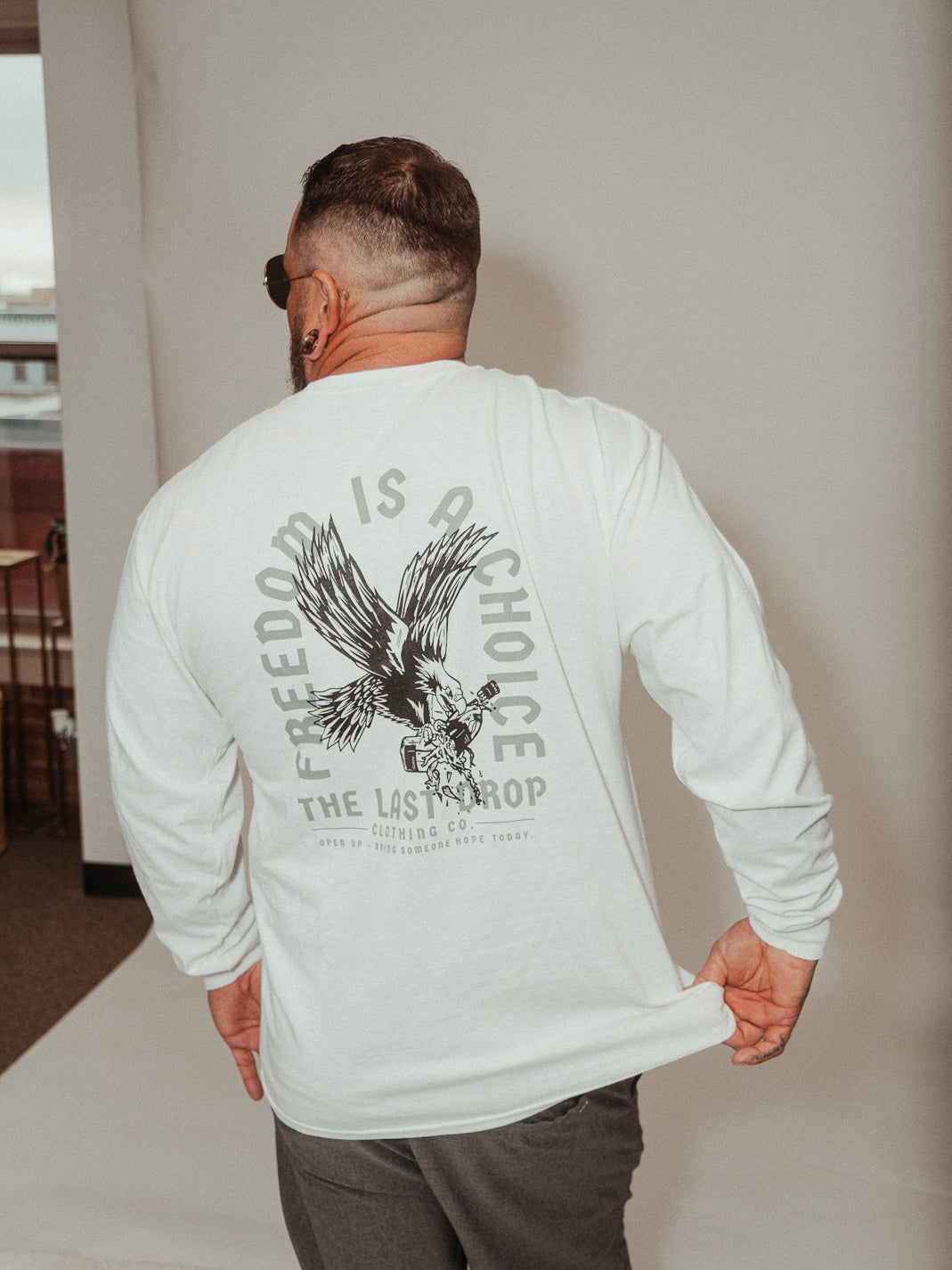 A man showcasing his strength and independence in a white long-sleeve shirt embellished with a powerful eagle design.