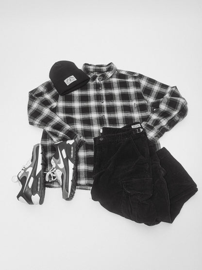 A black flannel shirt, black pants and a woven embroidered patch hat.