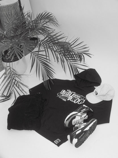 A black and white photo showcasing the comfort and style of a black t-shirt, sneakers, Trademark Black Y2K Hoodie, and a plant.