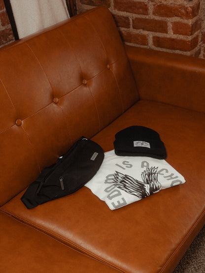 A woven embroidered patch beanie and a t-shirt on a brown leather couch.